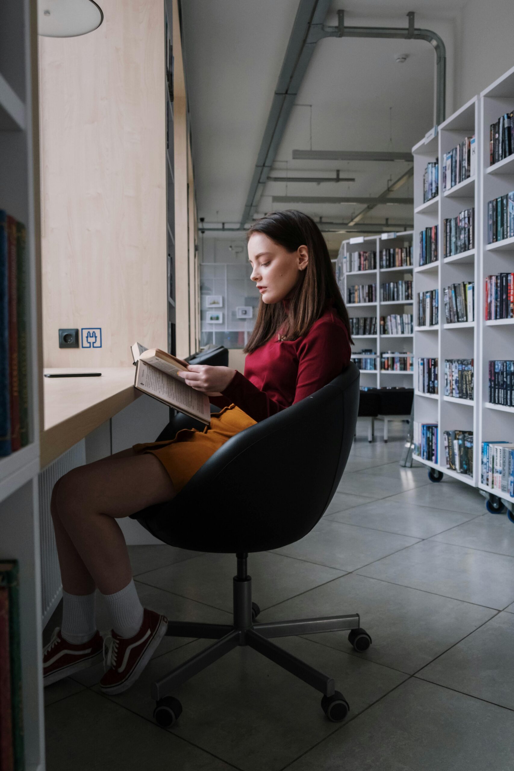 A teenage girl immersed in reading a book while sitting in a modern library.